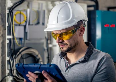 man-electrical-technician-working-switchboard-with-fuses-uses-tablet_169016-24007